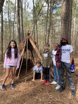 students next to natural shelter in woods